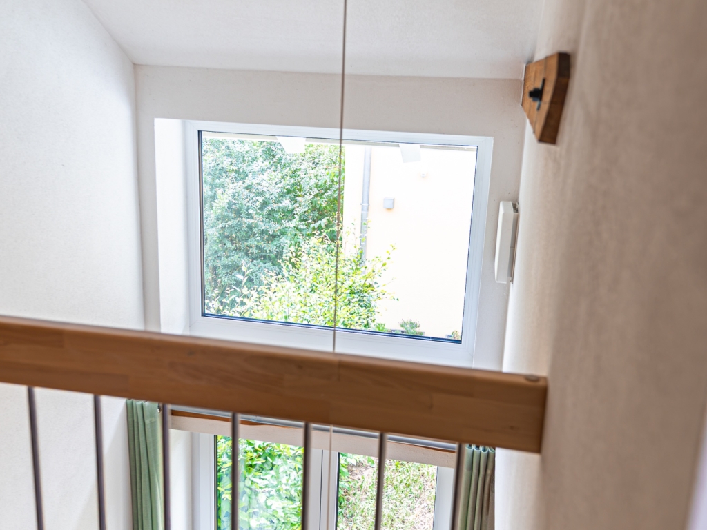 Ferienwohnung 6: Blick von der Galerie durch die Geländerstäbe zu einem Fenster mit Grün im Hintergrund
