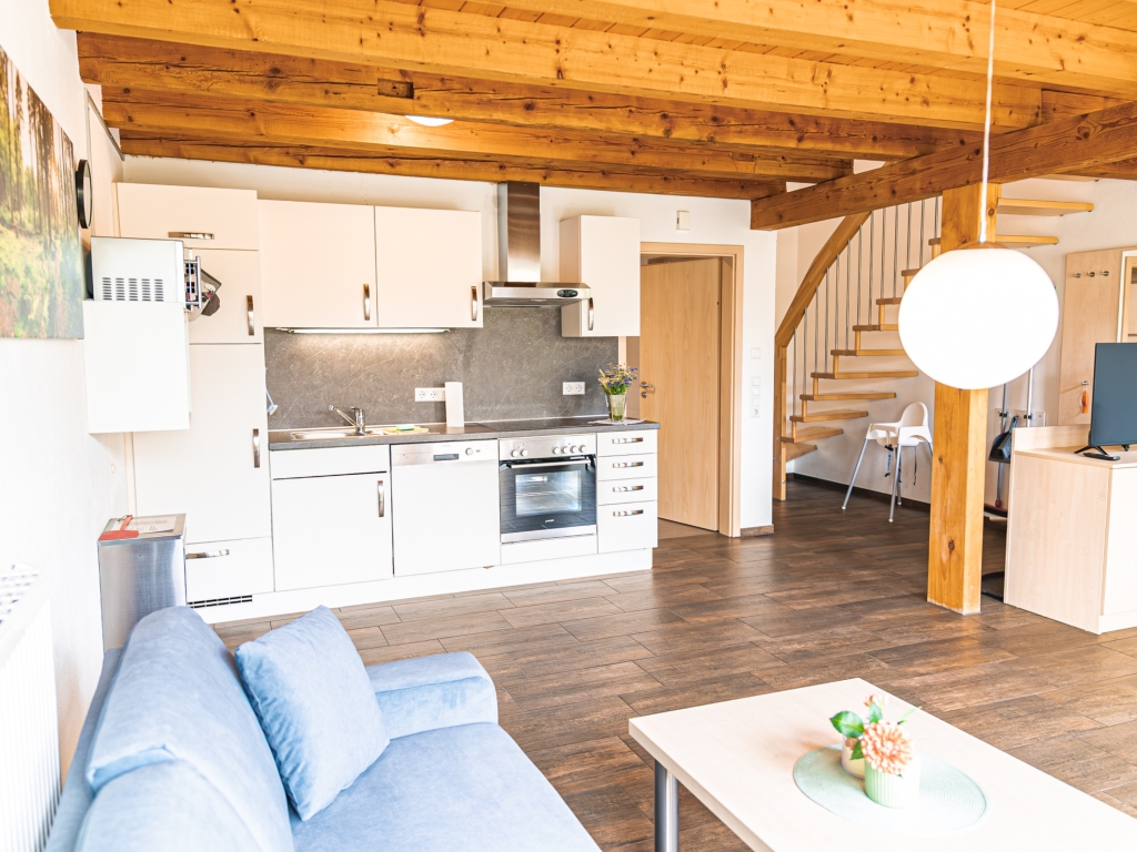 Ferienwohnung 6: Küchenzeile mit Backofen und Dunstabzugshaube, daneben Sofa und gewendelte Holztreppe