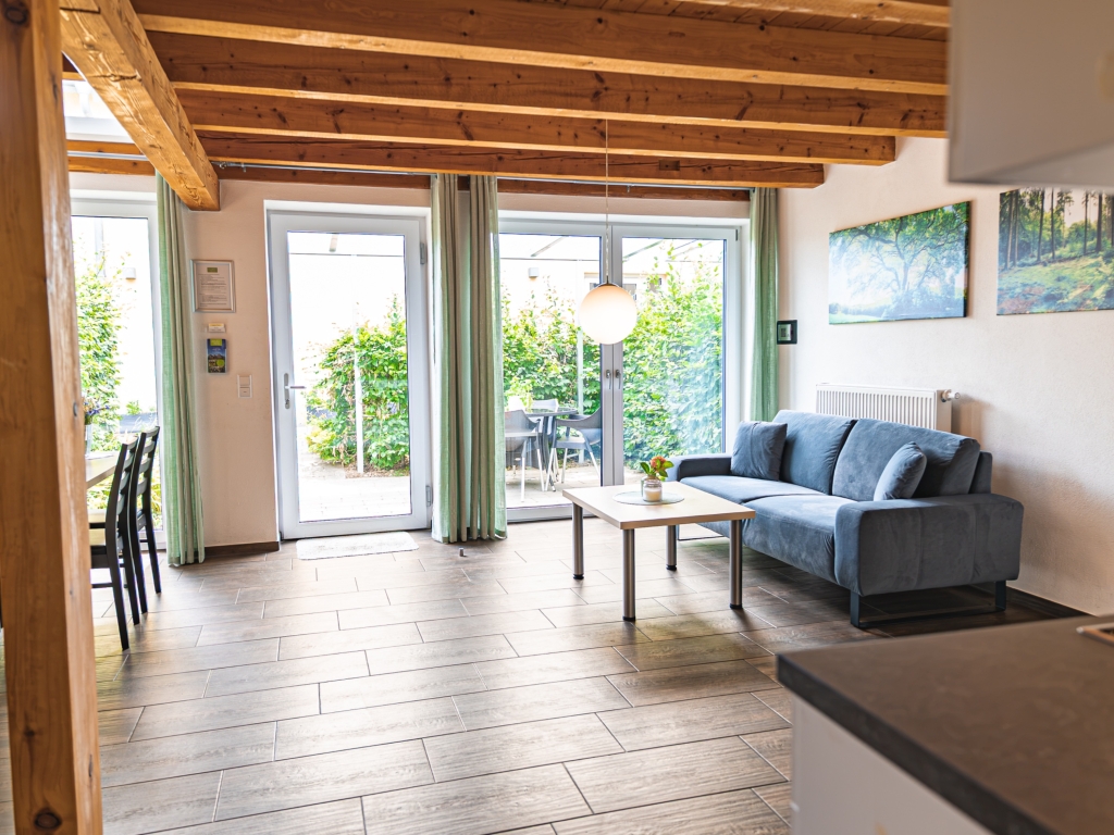 Ferienwohnung 6: Heller Wohnbereich mit Sofa und Couchtisch vor Terrassentüren mit Blick ins Grüne