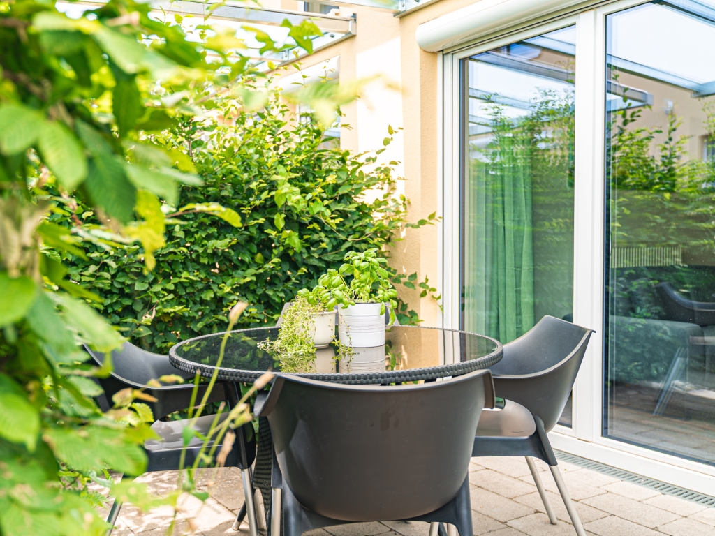 Ferienwohnung 6: Terrasse mit Tisch und dunklen Stühlen, umgeben von grünen Hecken