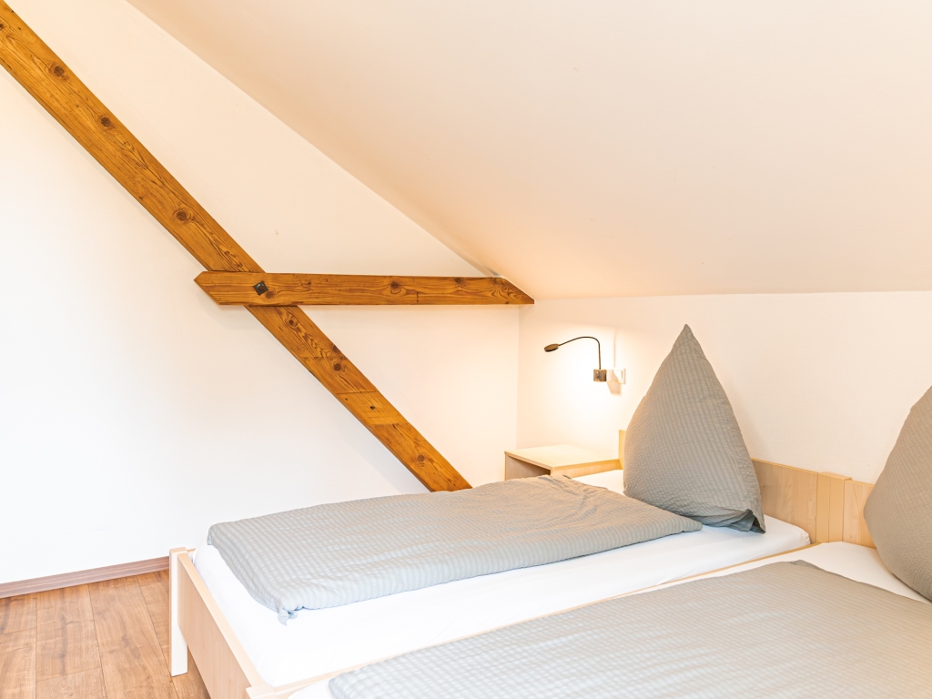 Ferienwohnung 7: Schlafzimmer mit zwei Betten in hellblauer Bettwäsche, Leselampen und Dachbalken