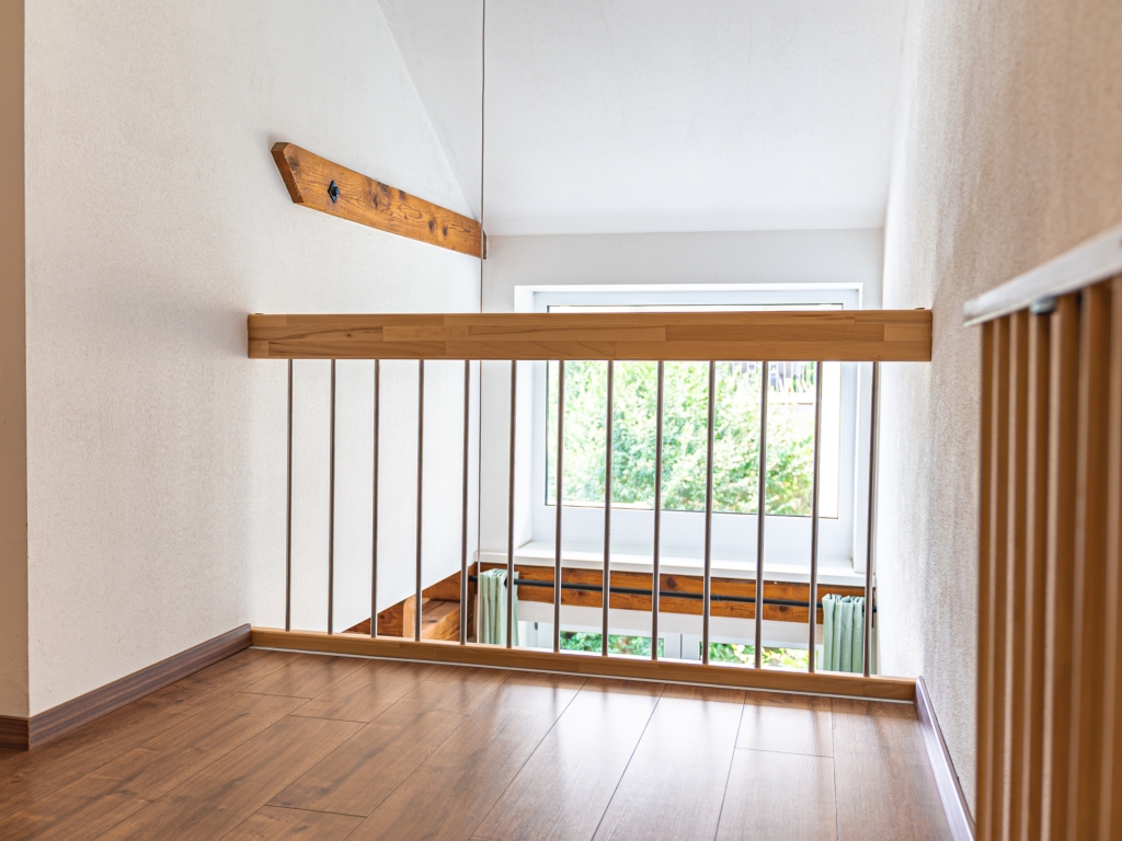Ferienwohnung 7: Galerie mit Holzboden und Geländer, dahinter ein Fenster mit Blick ins Grüne