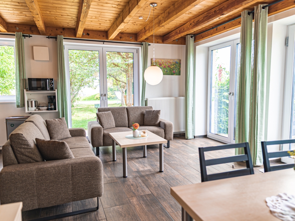 Ferienwohnung 7: Wohnbereich mit Sofa, Couchtisch, Regal und Terrassentüren mit grünen Vorhängen