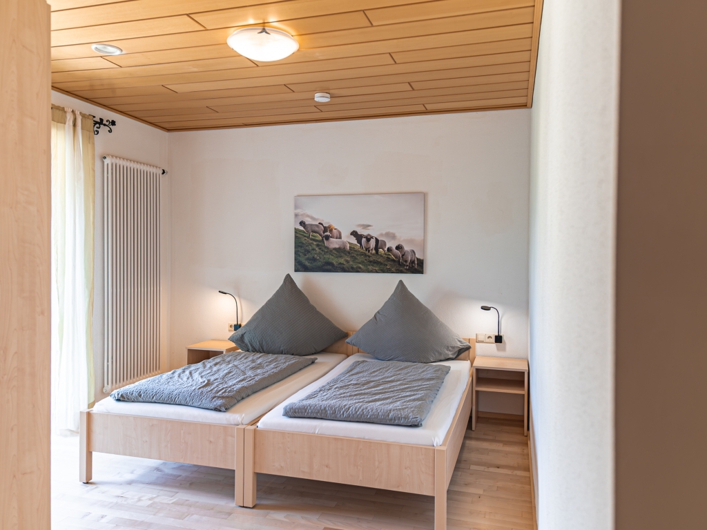 Ferienwohnung 8: Schlafzimmer mit Doppelbett, grauer Bettwäsche, Nachttischlampen und Holzdecke