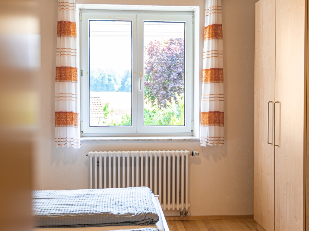 Ferienwohnung 8: Schlafzimmer mit Doppelbett, Kleiderschrank und Fenster mit gestreiften Vorhängen