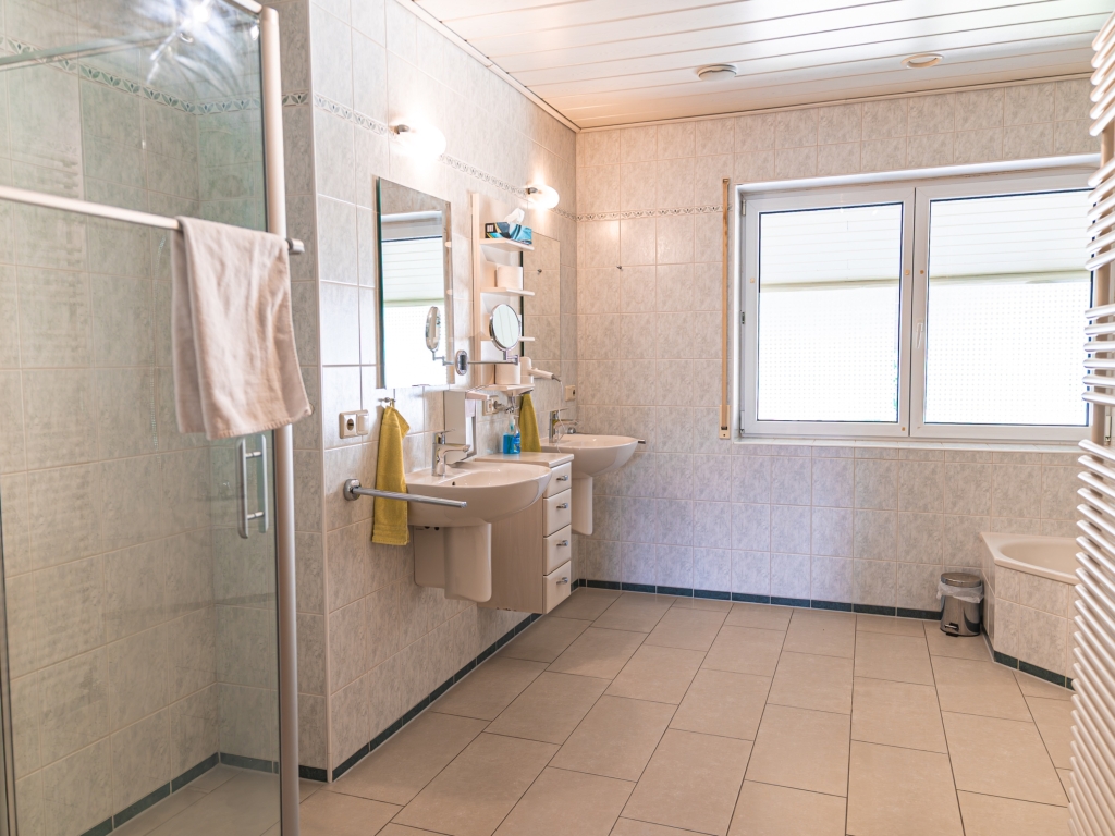 Ferienwohnung 8: Helles Badezimmer mit Dusche, Waschbecken, Spiegel, Fenster und hellem Fliesenboden