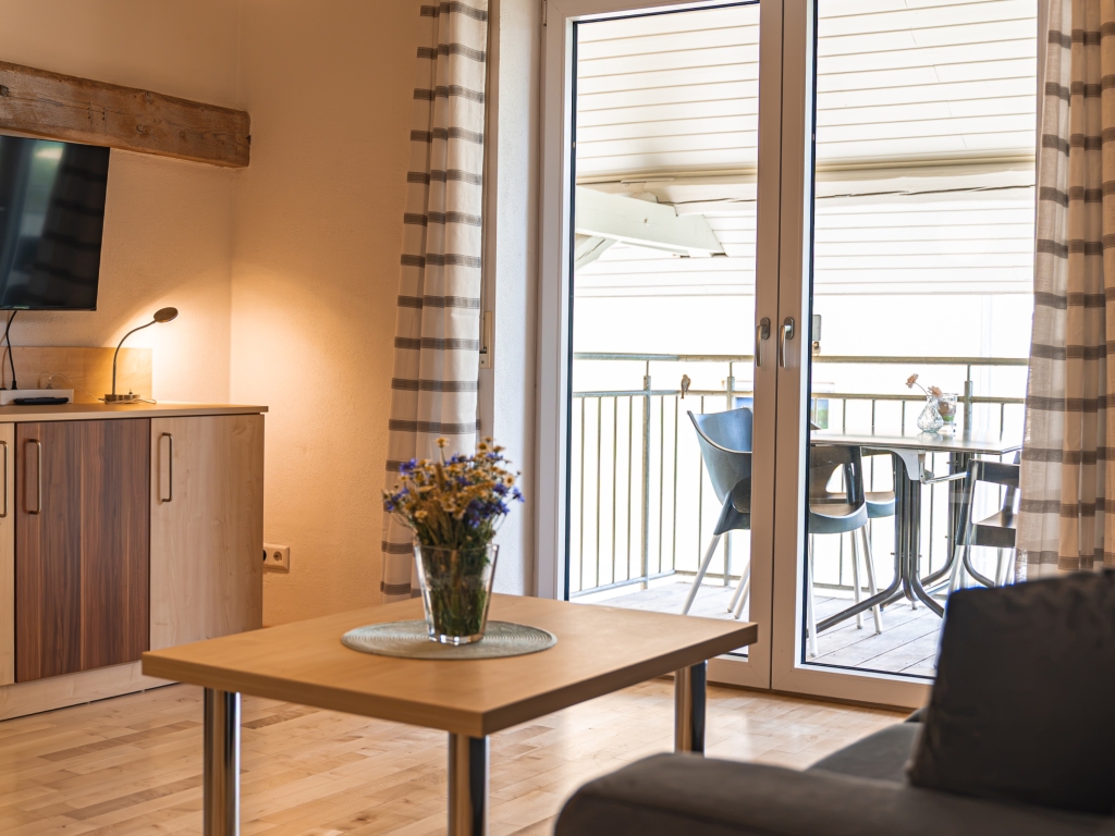 Ferienwohnung 8: Wohnbereich mit Couchtisch, Sessel und Fernseher, Balkontür mit Zugang zum Balkon