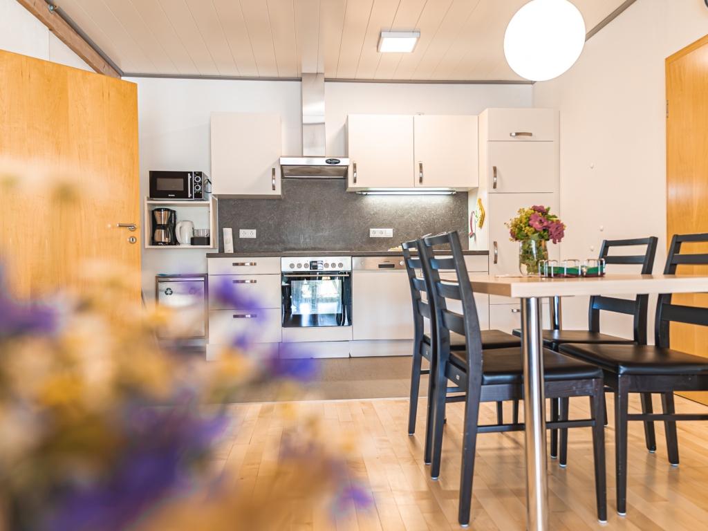 Ferienwohnung 8: Küche mit weißer Küchenzeile, Herd, Dunstabzug, Mikrowelle und Essplatz mit Stühlen