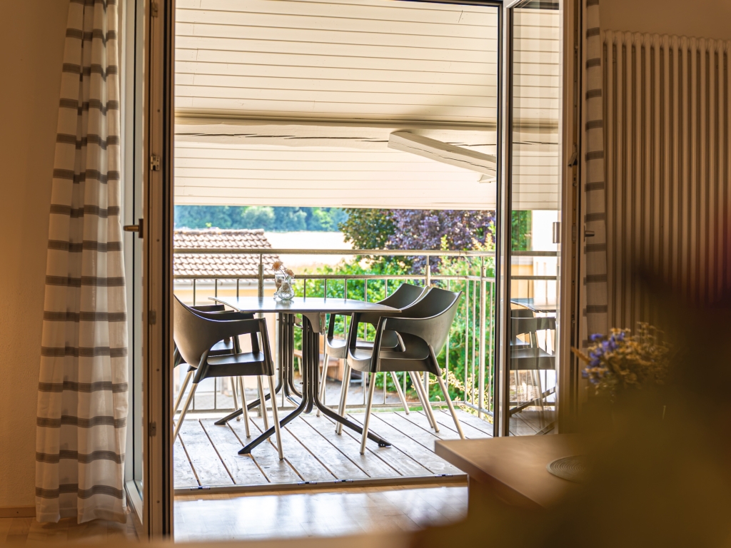 Ferienwohnung 8: Blick durch die offene Balkontür auf den Balkon mit Tisch, Stühlen und grünem Ausblick