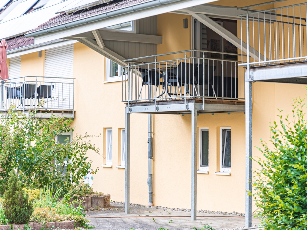 Ferienwohnung 8: Blick durch die offene Balkontür auf den Balkon mit Tisch, Stühlen und grünem Ausblick