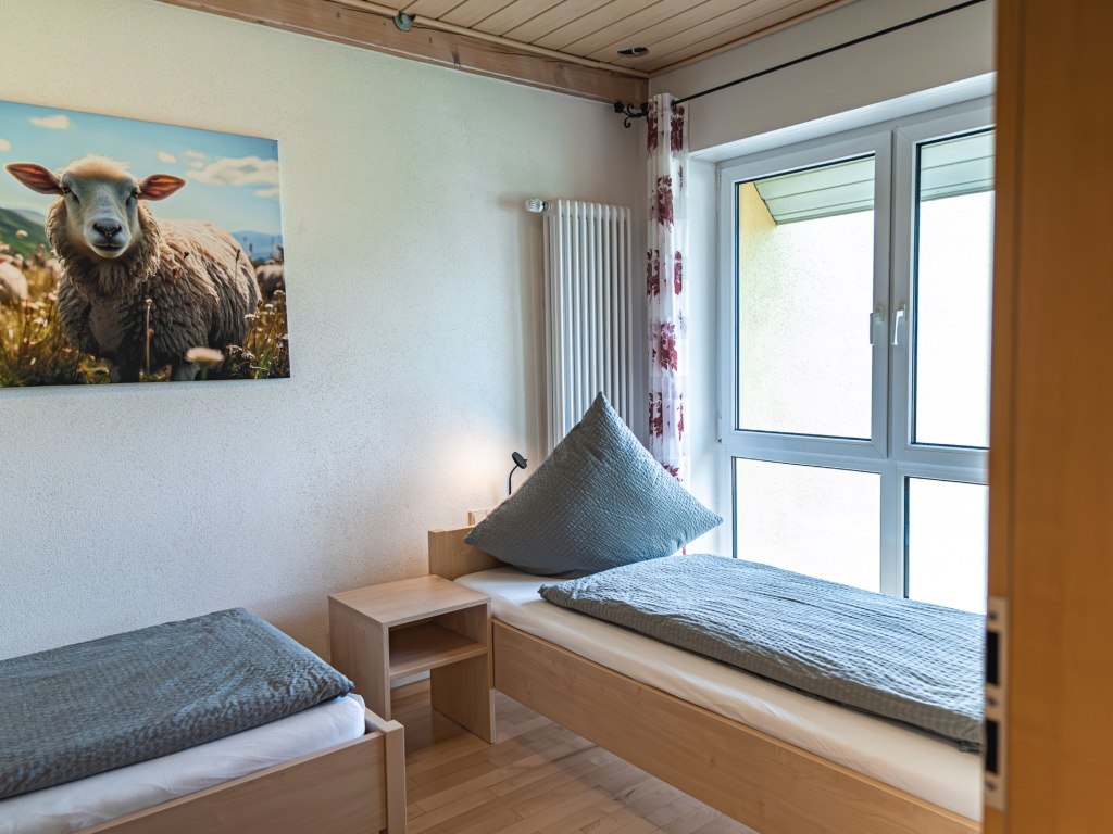 Ferienwohnung 9: Schlafzimmer mit Einzelbetten, Nachttisch und großem Schafbild an der Wand neben dem Fenster