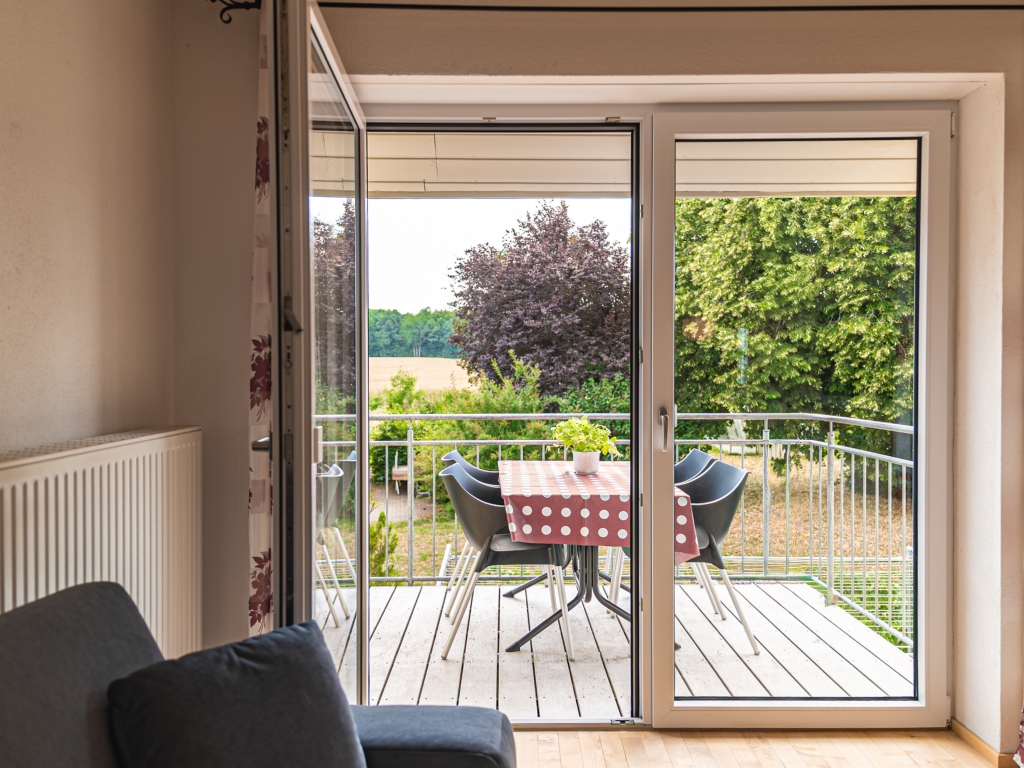 Ferienwohnung 9: Blick durch die offene Balkontür auf den Balkon mit Tisch, Stühlen und grünem Ausblick