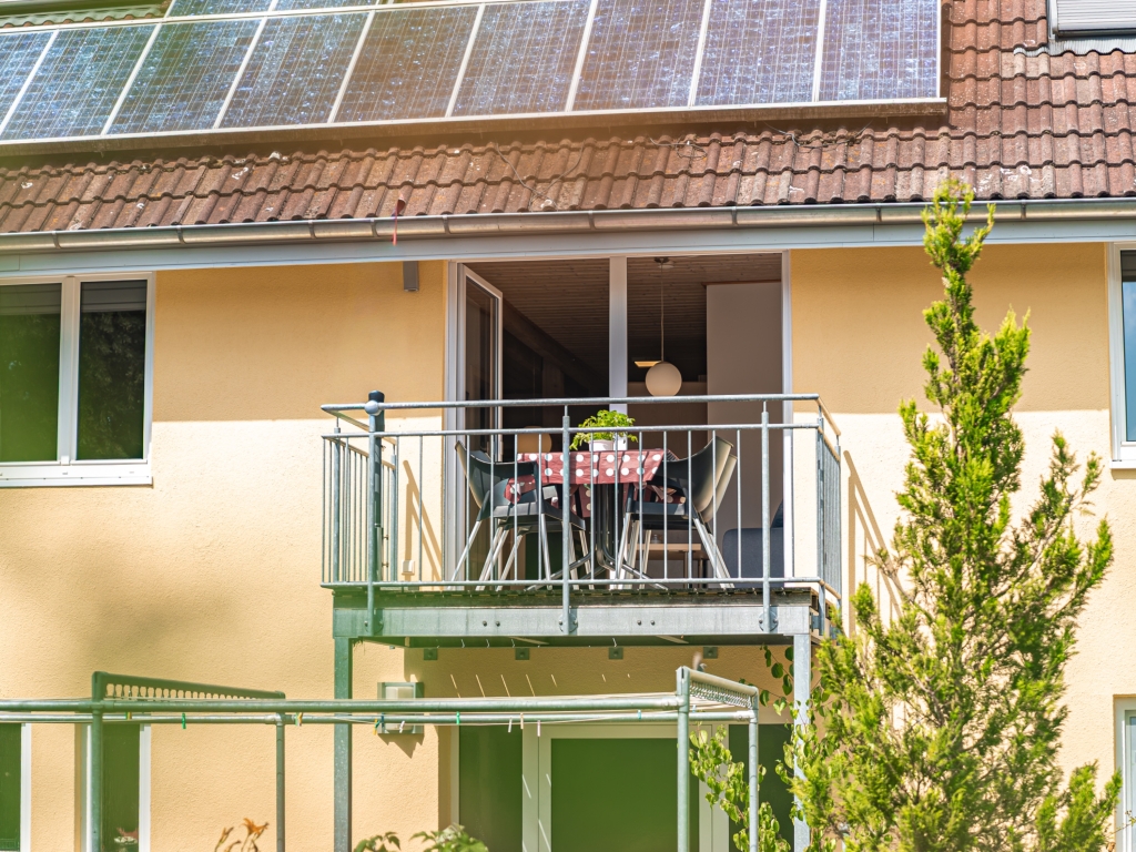 Ferienwohnung 9: Außenansicht des gelben Hauses mit Balkon, Tisch und Stühlen und Photovoltaikmodulen auf dem Dach